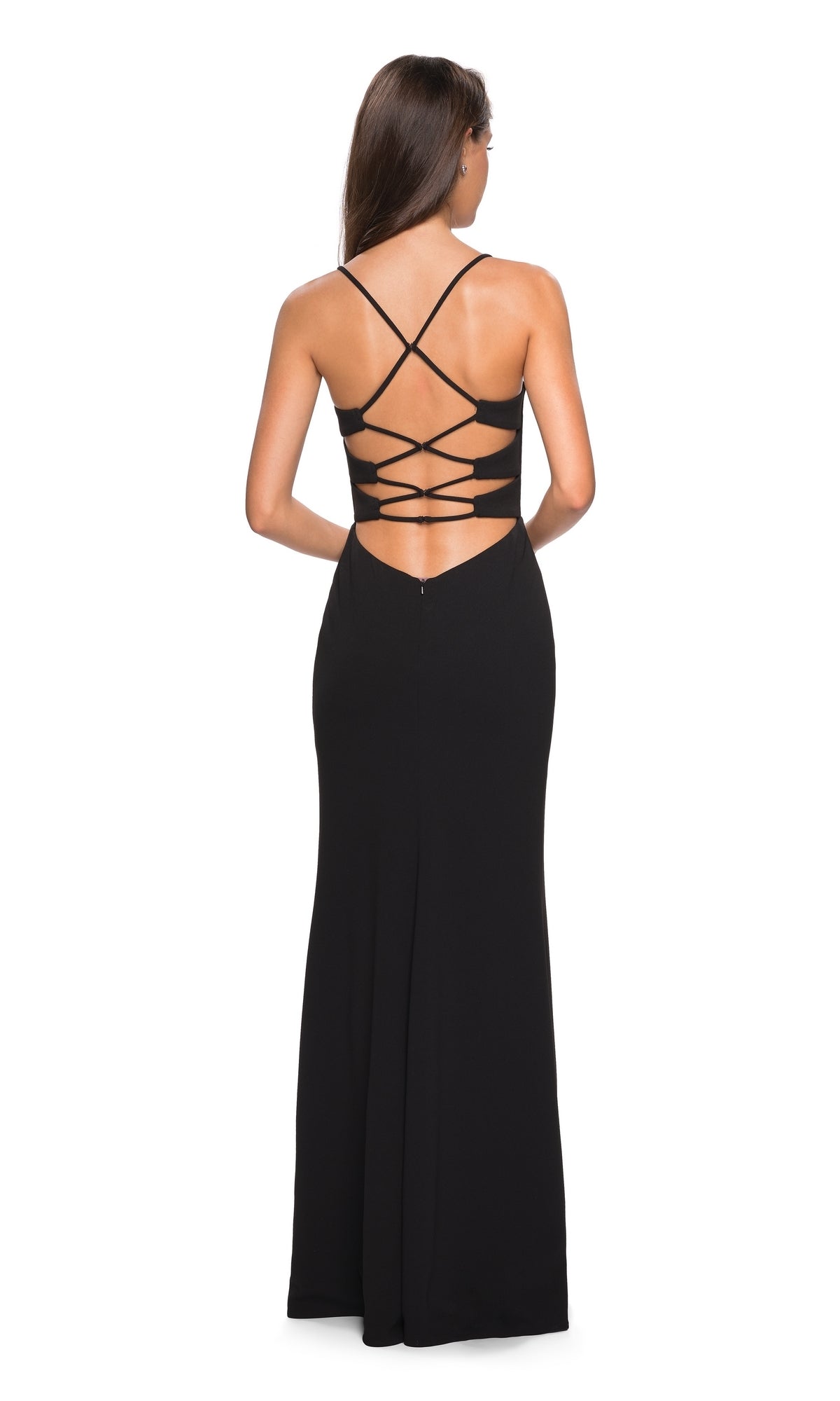 A woman stands facing away from the camera in the La Femme Strappy Open-Back Jersey Prom Dress 26940, a long black gown with crisscross straps and an open back.